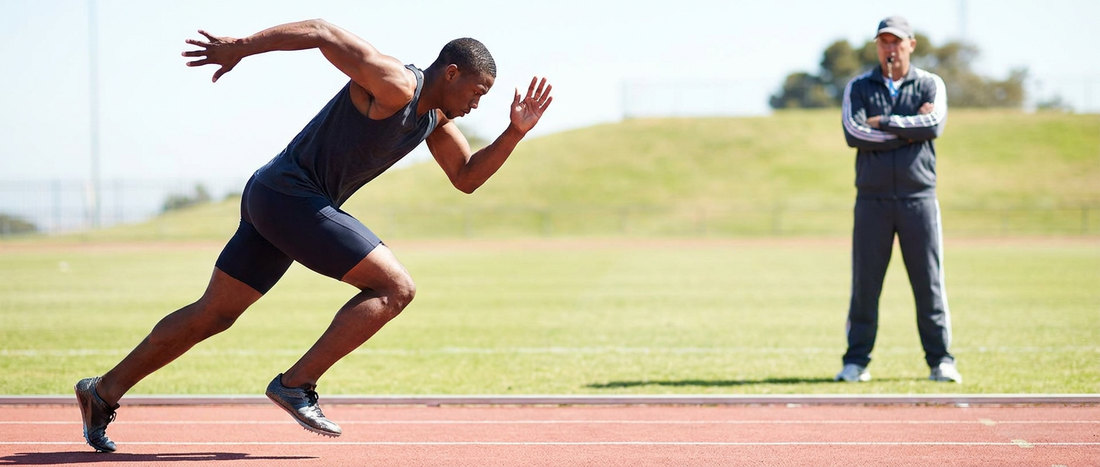 A sprinter running with a coach watching from the background